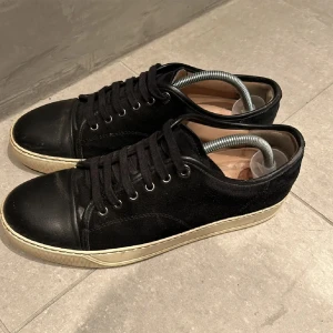 Lanvin - Snygga svarta sneakers från Lanvin med snörning och en stilren design. Skorna har en kombination av skinn och mocka vilket ger en lyxig känsla. Perfekta för en trendig look. Jävligt laidback.