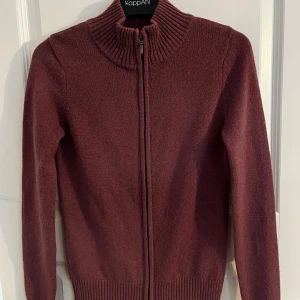 Vinröd full zip  - Säljer en stilren vinröd kofta från wool overs med dragkedja framtill. Den har en ribbad krage och långa ärmar, perfekt för kyligare dagar. Passar både till vardags och lite finare tillfällen. 