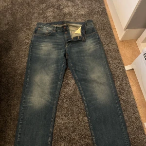 Blå jeans från Nudie Jeans - Säljer ett par snygga blå jeans från Nudie Jeans med en klassisk femficksdesign.  tillverkade i 100% bomull. Perfekta för en avslappnad stil. Modellen på jensen heter Rad Rufus Streaky Worn!