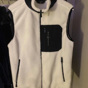 Vit fleeceväst från Sail Racing - Säljer en vit fleeceväst från Sail Racing med svart dragkedja och bröstficka. Västen har en hög krage och är perfekt för kyliga dagar. Den har en stilren design med kontrasterande detaljer. Har du frågor eller funderingar hör av dig! (Kan mötas upp) mvh Oldmoneyclooset!