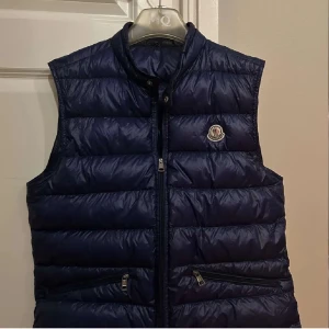 Moncler väst - Säljer min Moncler väst som är för stor på mig.        Skick är 7/10 ett litet hål på ryggen som syns knappt och är enkelt o laga skriv för flera frågor✌️köp vid PostNord tack!