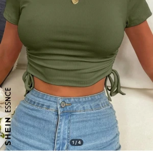 Olivgrön ribbad croppad topp från SHEIN - Snygg olivgrön ribbad topp från SHEIN. Den är croppad med knytband i sidorna och har korta ärmar. Perfekt för en trendig look!