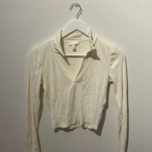 Vit ribbad tröja från H&M - Säljer en stilren vit ribbad tröja från H&M. Tröjan har en v-ringad design med en liten krage och långa ärmar. Perfekt för vår och sommar!