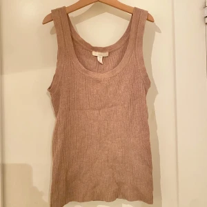 Beige ribbad stickad linnetopp - Säljer en stilren beige ribbad linnetopp. Perfekt för varma dagar med sin ärmlösa design och mjuka material. Enkelt att matcha med olika outfits.