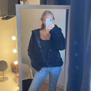 Svart pälsjacka med huva - Säljer en mysig svart pälsjacka med huva. Jackan har en loose passform och långa ärmar, perfekt för kyliga dagar. Den är stilren och enkel att matcha med olika outfits. Perfekt för höst och vinter! Man kan vända den ut och in! Skulle säga storlek S.