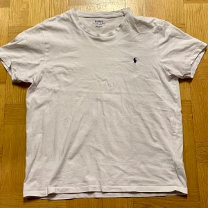 Polo Ralph Lauren T-shirt - Säljer en klassisk vit t-shirt från Polo Ralph Lauren med den ikoniska broderade loggan på bröstet, i det här fallet mörkblå. T-shirten är kortärmad och tillverkad i mjuk bomull för en bekväm passform. Säljer för att den är för liten. Kom gärna med frågor! Skickar inom ett dygn.