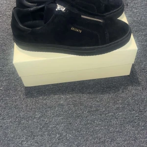 Svarta Axel Arigato - Snygga svarta sneakers i mocka från Axel Arigato med dragkedjedetalj på ovansidan. Skorna har en stilren design, Perfekta för en trendig look. Skorna säljs inte idag och har använt dom ett par gånger, pris kan diskuteras 