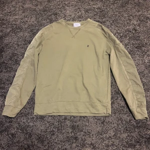 Olivgrön sweatshirt från Dondup - Säljer en stilren olivgrön sweatshirt från Dondup. Tröjan har långa ärmar och en liten broderad logotyp på bröstet. Perfekt för en avslappnad look.