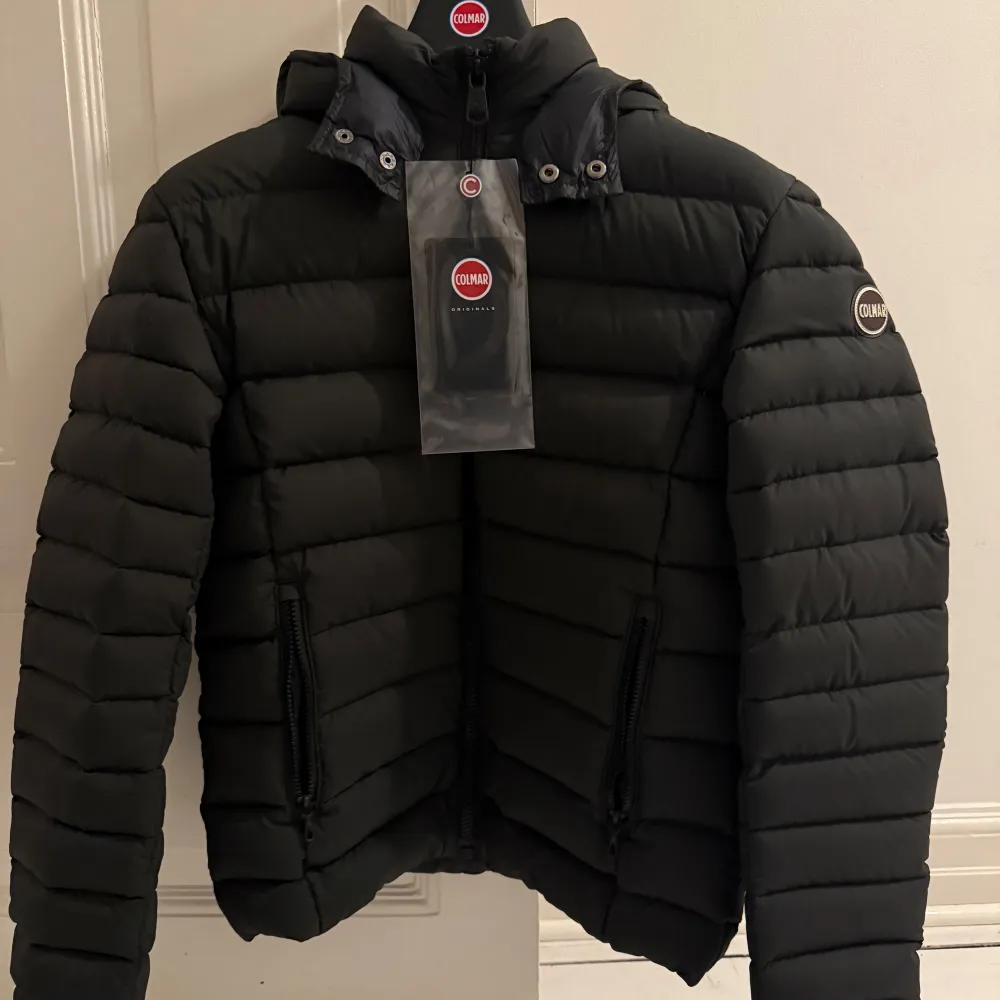 Säljer en snygg svart pufferjacka från Colmar. Jackan har en quiltad design med dragkedja och en hög krage för extra värme. Perfekt för kyliga dagar och har en stilren look med Colmar-logga på ärmen.. Takit.