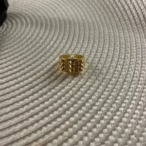 Guldfärgad ring med geometriskt mönster - Snygg guldfärgad ring med ett unikt geometriskt mönster. Ringen har en öppen design vilket gör den justerbar och bekväm att bära. Perfekt för att ge en edgy touch till din stil.