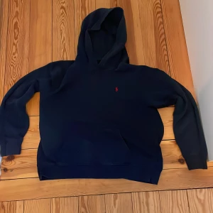 Svart hoodie från Polo Ralph Lauren - Säljer en stilren mörkblå hoodie från Polo Ralph Lauren. Den har en klassisk design med en liten röd logotyp på bröstet och en bekväm huva. Perfekt för en avslappnad look.