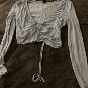 Ljusblå ribbad topp från Shein - Säljer en ljusblå ribbad topp från Shein med långa ärmar och knytning framtill. Toppen har en v-ringad design och är croppad för en trendig look. Perfekt för att lägga till en stilren touch till din garderob.