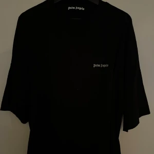 Svart t-shirt från Palm Angels - Helt ny svart t-shirt från Palm Angels i storlek M. Den är kortärmad och har en stilren design med Palm Angels-loggan tryckt på bröstet. Perfekt för en casual look eller att styla upp med accessoarer. T-shirten är i bra skick och redo för en ny äg