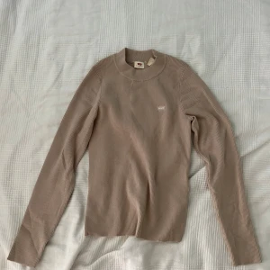Beige ribbad tröja från Levi's - Säljer en snygg beige ribbad tröja från Levi's i storlek M. Tröjan har en klassisk design med långa ärmar och en rund halsringning. 