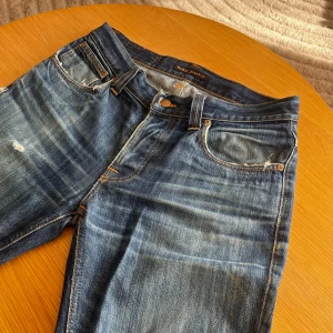 Blå jeans från Nudie Jeans - Säljer ett par snygga blå jeans i modellen Grim Tim från Nudie Jeans. Dom har några snygga slitningar som är diskreta. Pris kan diskuteras vid snabb affär!