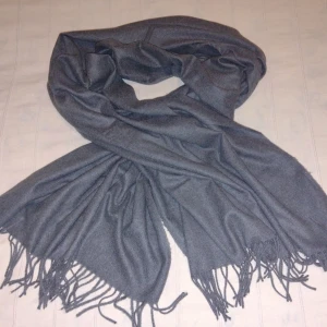 Oanvänd stor grå halsduk  - Oanvänd grå halsduk. Ca 180 cm.lång exkl. fransar och 73 cm bred. Mjuk och skön. 70% polyester och 30% viskos. Har aldrig använts men tvättats. 