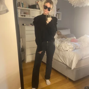 Svart stickad tröja från H&M - Säljer en snygg svart stickad tröja från Vera Moda. Den har långa ärmar och en cool volangdetalj på axlarna som ger den lite extra stil. Perfekt för höst och vinter när du vill hålla dig varm men ändå se trendig ut. Passar både till vardags och fest!