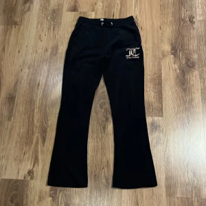 Svarta byxor från Juicy Couture - Snygga svarta byxor från Juicy Couture med logga på benet. Byxorna har en bekväm passform och är perfekta för en avslappnad stil. De är tillverkade i ett mjukt material och har en dragsko i midjan för justerbar passform. Byxorna är i storlek 12-13 men passar även 13-14! Byxorna är i ny skick och är använda ca 2 gånger.