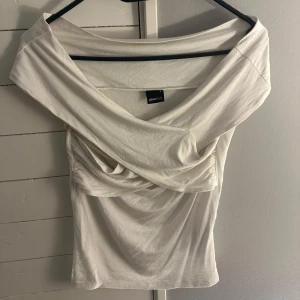 Vit offshoulder topp från Gina Tricot - Säljer en stilren vit offshoulder topp från Gina Tricot. Toppen har en elegant drapering framtill och är tillverkad i ett mjukt material. Strl S🩷🩷