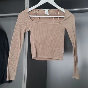 RIbbad topp från Stradivarius - Säljer en snygg beige/brun/mullvad croppad & ribbad topp från Stradivarius. Toppen har långa ärmar och en fyrkantig halsringning. Perfekt för en stilren look med en tight passform 👌 Passar bra till både jeans och kjol.