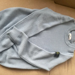 Stone island sweatshirt  - Säljer en stilren ljusblå tröja från Stone Island. Tröjan har en broderad logga på ärmen och är tillverkad i ett mjukt material. Perfekt för en avslappnad stil.