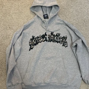 Grå hoodie från Sweet SKTBS - Säljer en grå hoodie från Sweet SKTBS med svart och vit text på bröstet. Den har en klassisk design med huva och dragsko samt en stor magficka. Perfekt för en avslappnad stil.