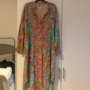 Färgglad kimono med mönster - Säljer en färgglad kimono med ett psykedeliskt mönster i rosa, blått, gult och grönt. Kimonon har långa ärmar och knappar hela vägen. Perfekt för att sticka ut med sin unika stil! 