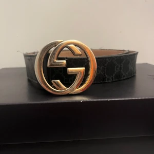 Svart bälte med GG-spänne - Snyggt svart bälte från Gucci med det ikoniska GG-mönstret och ett stort, glänsande GG-spänne i guld. Perfekt för att ge en lyxig touch till din outfit. PRISTE KAN DISKUTERA VID SNABB AFFÄR!!💰
