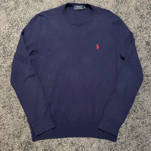 Mörkblå tröja från Ralph Lauren - Säljer en stilren mörkblå tröja från Ralph Lauren med det klassiska röda broderade logotypen på bröstet. Tröjan har rund hals och långa ärmar, perfekt för en avslappnad men snygg look. Passar bra till jeans! Storlek M.