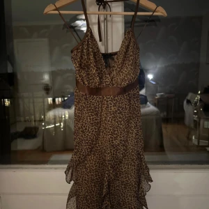 Leopardmönstrad klänning med volangdetaljer - Snygg leopardmönstrad klänning med smala axelband och volangdetaljer. Klänningen har en knytning i midjan och nacken. Den är lätt och luftig, perfekt för fest.