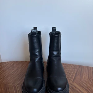 Svarta boots  - Snygga svarta  boots med en robust sula. De har en klassisk design med elastiska paneler på sidorna för enkel på- och avtagning. Perfekta för en stilren look. Storlek 38