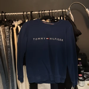 Blå sweatshirt från Tommy Hilfiger - Säljer en snygg blå sweatshirt från Tommy Hilfiger med deras ikoniska logga på bröstet. Tröjan har långa ärmar och en rund halsringning. Perfekt för en avslappnad stil.