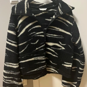 Svart och vit teddyjacka från H&M - Säljer en cool svart och vit teddyjacka från H&M med zebramönster. Jackan har en dragkedja framtill och är långärmad. Perfekt för att hålla sig varm och stilren under kyligare dagar. 