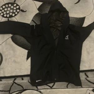 Svart vindjacka från Haglöfs priset kan diskuteras  - Säljer en svart vindjacka från Haglöfs med huva och dragkedja. Perfekt för blåsiga dagar. Jackan har en stilren design och är tillverkad i syntetmaterial.