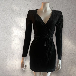 Svart omlottklänning - & Other Stores elegant svart omlottklänning med långa ärmar och knytband i midjan. Klänningen har en subtil glittrig effekt och en v-ringad halslinje som ger en sofistikerad look.  Storlek: usa 2/ EUR 34 men passar till 36 också. 