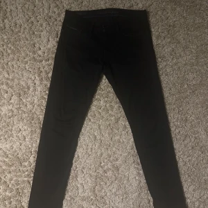 Svarta jeans från Calvin Klein - Snygga svarta jeans från Calvin Klein med klassisk design. De har en knapp och dragkedja framtill samt fickor både fram och bak. Perfekta för en stilren look.