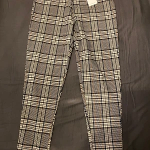 Rutig byxa från Frilivin - Snygga rutiga byxor från Frilivin i beige, svart och vit. Byxorna har en klassisk stil med knappar i midjan och är perfekta för en stilren look. Passar bra till både vardag och mer uppklädda tillfällen. Oanvända, endast provade.