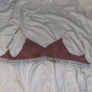 Rosa bralette från Calvin Klein - Säljer en snygg rosa bralette från Calvin Klein med justerbara axelband och elastiskt band med logotypen CK One. Perfekt för en bekväm och stilren look.