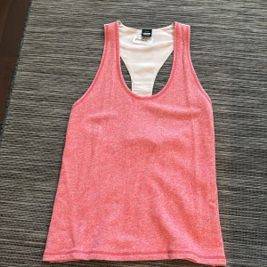 Rosa linnetopp från DRDENIM - Säljer en snygg rosa linnetopp från DRDENIM med brottarrygg i vitt. Perfekt för varma sommardagar eller träning. Toppen har en enkel och stilren design.