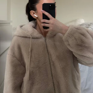 Beige teddyjacka med dragkedja - Mysig beige teddyjacka med dragkedja och huva. Perfekt för kyliga dagar med sin fluffiga och varma design. Jackan har en avslappnad passform och ribbade muddar vid ärmslut och nederkant. Från bershka köpt för ett par år sedan sparsamt använd