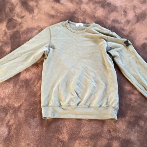  Stone Island  - Säljer en olivgrön tröja från Stone Island Junior. Tröjan har långa ärmar och en rund halsringning. Den är dekorerad med det ikoniska Stone Island-märket på ärmen. Hör av dig vid frågor.