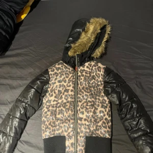 Leopardmönstrad jacka från Coolcat - Säljer en cool leopardmönstrad jacka från Coolcat med svarta quiltade ärmar och huva med fuskpäls. I bra skick, passar. XXS-S