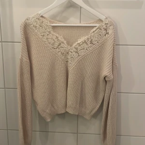 Beige stickad tröja med spetsdetaljer - Säljer en snygg beige stickad tröja med vackra spetsdetaljer vid halsringningen. Tröjan har en avslappnad passform och långa ärmar. Den är både stilren och bekväm, ett måste i garderoben!