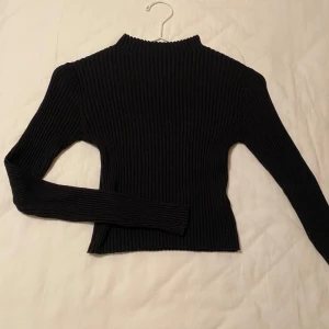 Svart ribbad tröja - Säljer en stilren svart ribbad tröja med långa ärmar. Perfekt för en minimalistisk look och passar bra till både jeans och kjol. Tröjan har en högre hals och är gjord i ett mjukt material. Kontakta mig om du har frågor ☺️