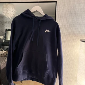 Mörkblå hoodie från Nike - Säljer en snygg mörkblå hoodie från Nike med klassisk logga på bröstet. Tröjan har en bekväm passform med känguruficka och justerbar huva. Perfekt för en avslappnad stil. Den är väl använd och därav priset. Storlek M 