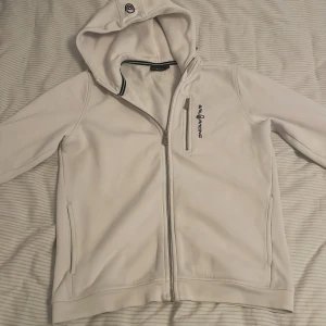 Vit hoodie från Sail Racing - Säljer en stilren vit hoodie från Sail Racing med dragkedja och huva. Perfekt för en avslappnad look. Den har en broderad logga på bröstet och är tillverkad i mjukt material för extra komfort. Lite fläck på Baksidan längst ner på tröjan men inget man lägger märke till 170 i ungdoms storlek skulle säga att den passar S men bäst passar den xs köpt på kidsbrandstore kvitto finns inte skriv för mer info 