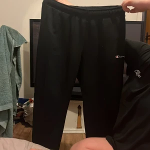 Svarta mjukisbyxor från Champion - Säljer ett par svarta mjukisbyxor från Champion. Byxorna har en elastisk midja och är perfekta för en avslappnad stil. Champion-loggan är tryckt på sidan av byxorna.