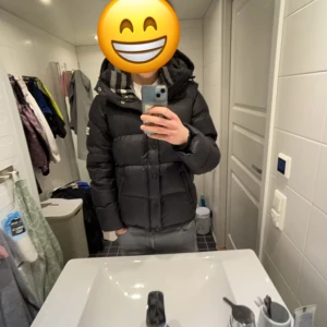 Svart burberry jacka - Säljer en burberry pufferjacka med dragkedja och knappar. Jackan har en hög krage och långa ärmar, perfekt för kyliga dagar. Den är både stilren och funktionell.