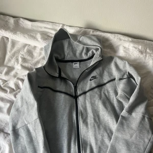 Grå hoodie från Nike - Säljer en Nike Tech Fleece som brukar kosta runt 1000kr online – men jag säljer den för bara 500kr! Den är i superbra skick, nästan som ny, och använd endast en gång. Den är både snygg och funktionell, perfekt för att hålla värmen utan att förlora stil. Storlek M, passar både för träning och vardagsbruk. Ett grymt kap om du är ute efter kvalitet till ett bra pris! Först till kvarn, så hör av dig snabbt om du vill slå till! Priset kan diskuteras 