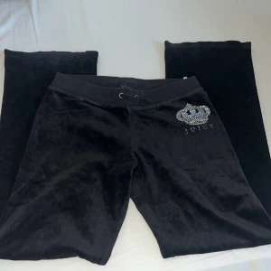 Svarta bootcut mjukisbyxor från Juicy Couture - Säljer snygga svarta mjukisbyxor från Juicy Couture då de blivit för små för mig. Byxorna har ett tryck av en glittrig krona med texten 'Juicy' på framsidan. Byxorna har snörning i midjan för justerbar passform. Perfekta för en avslappnad och stilren look. 🤗